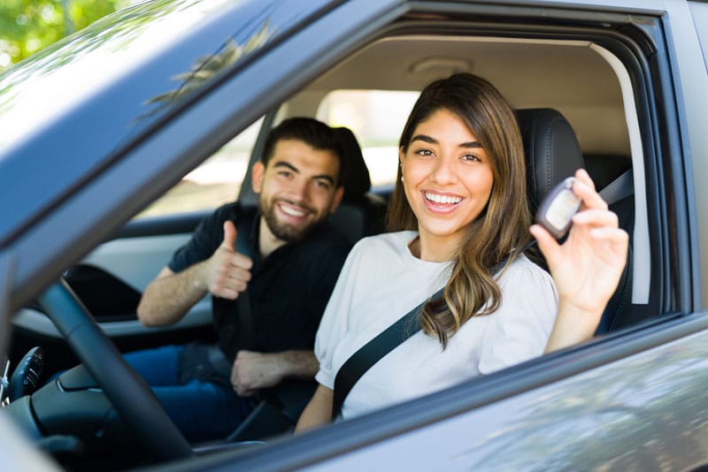 A couple in their new car, holding keys with a thumbs up